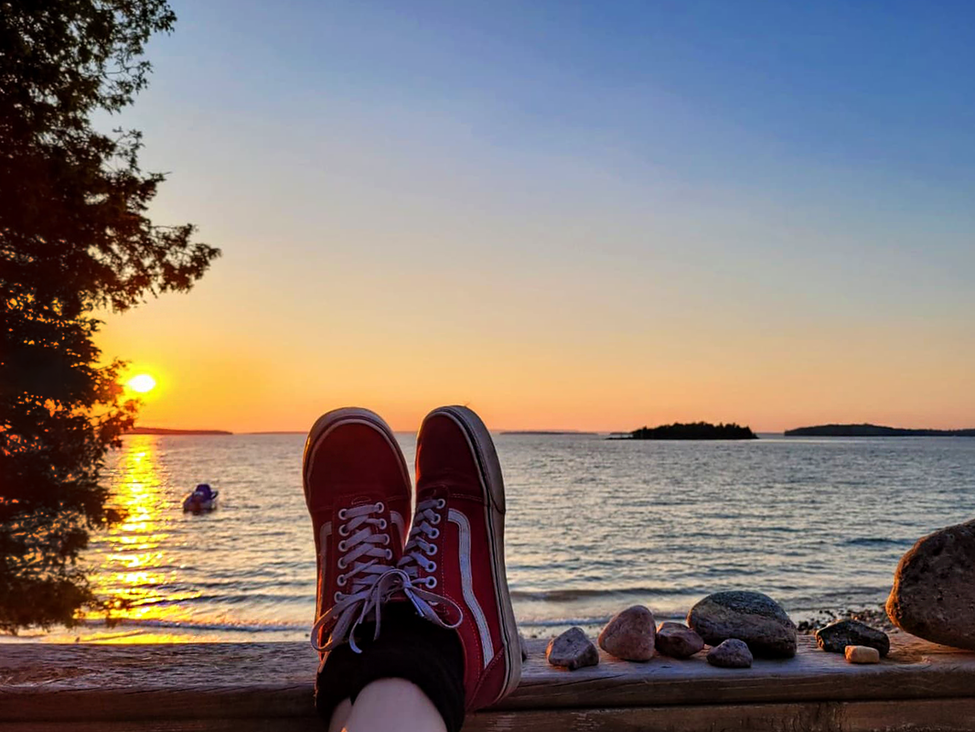 Feet resting on a ledge in front of a sunset over the beach